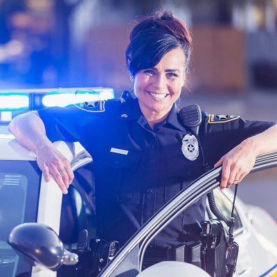 A happy police woman standing next to her police car.